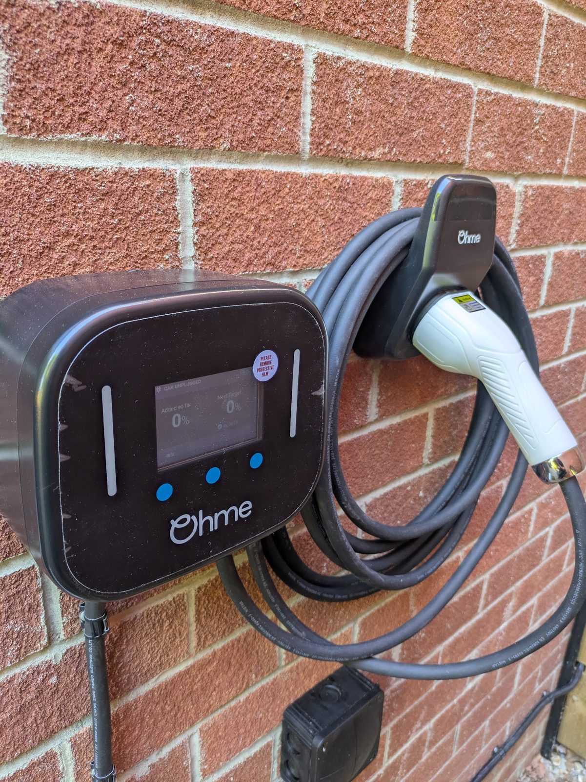 An Ohme EV charger with its cable coiled on a brick wall